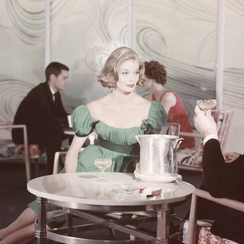 In the Caribbean Lounge aboard the Santa Rosa drinking champagne model wearing green evening dress of silk chiffon over...
