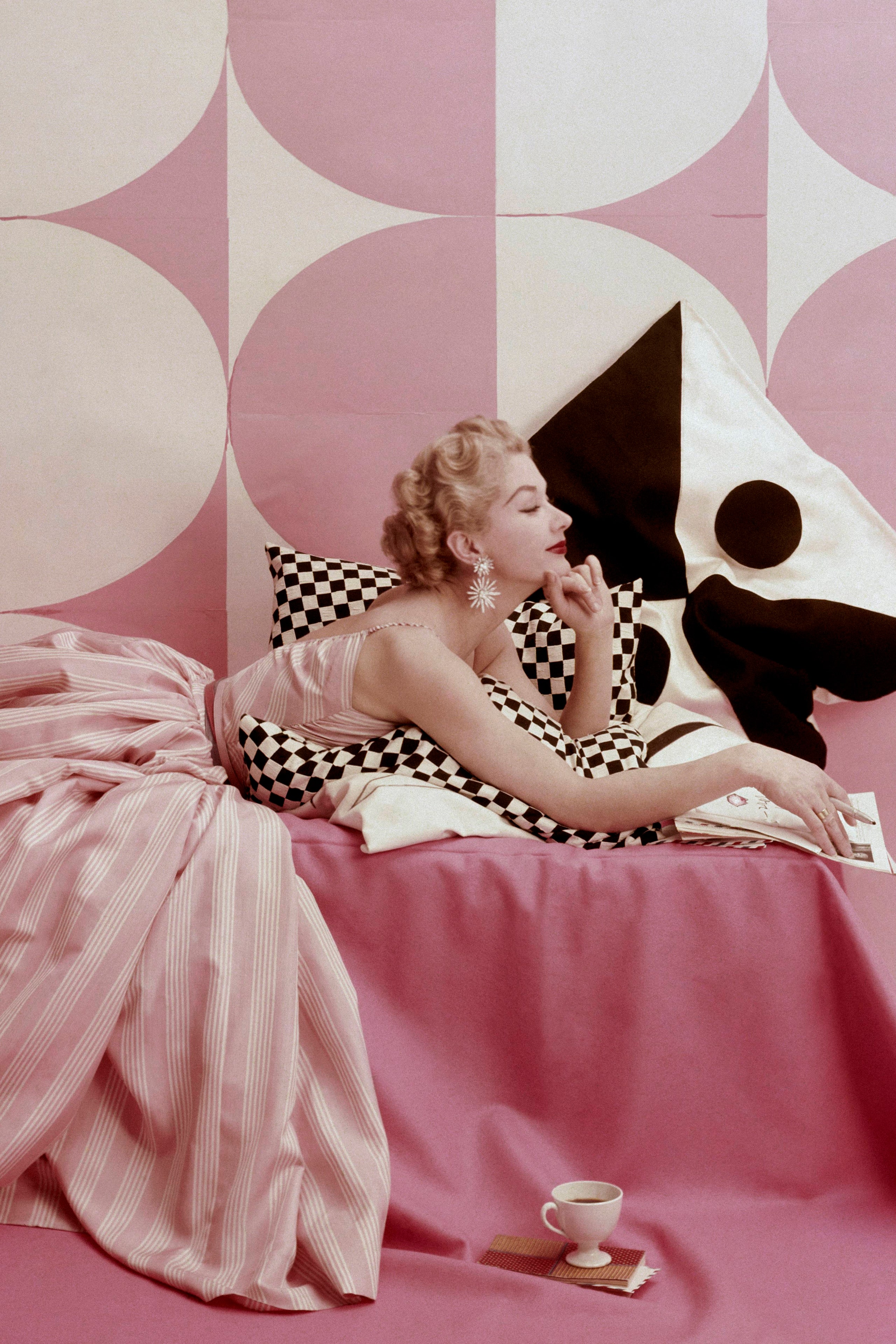 Model Lisa Fonssagrives lounging on bed wearing Claire McCardell's pink and white striped dress.