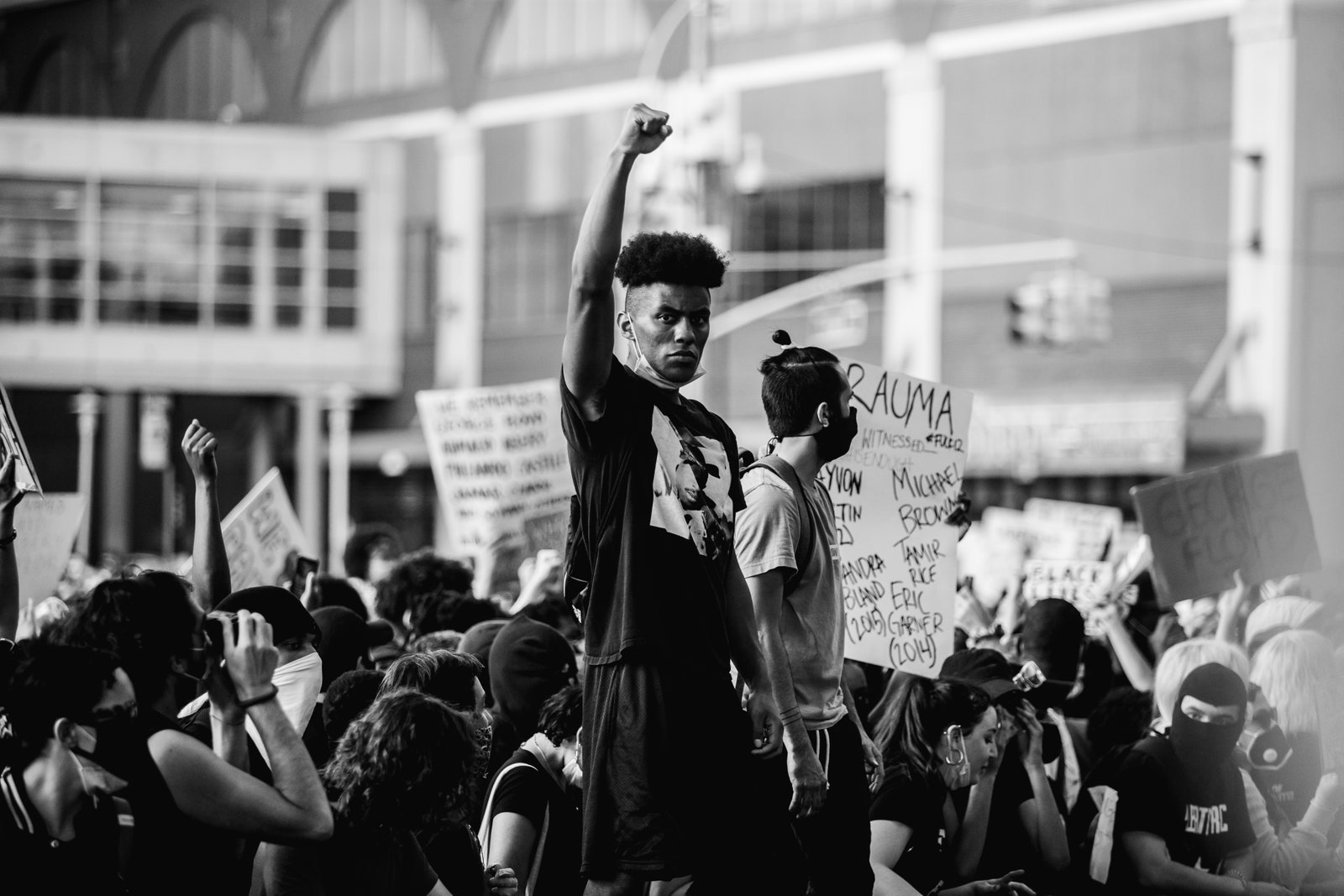 Молодой афроамериканец стоит с поднятым вверх кулаком в знак солидарности с другими протестантами во время митинга в...