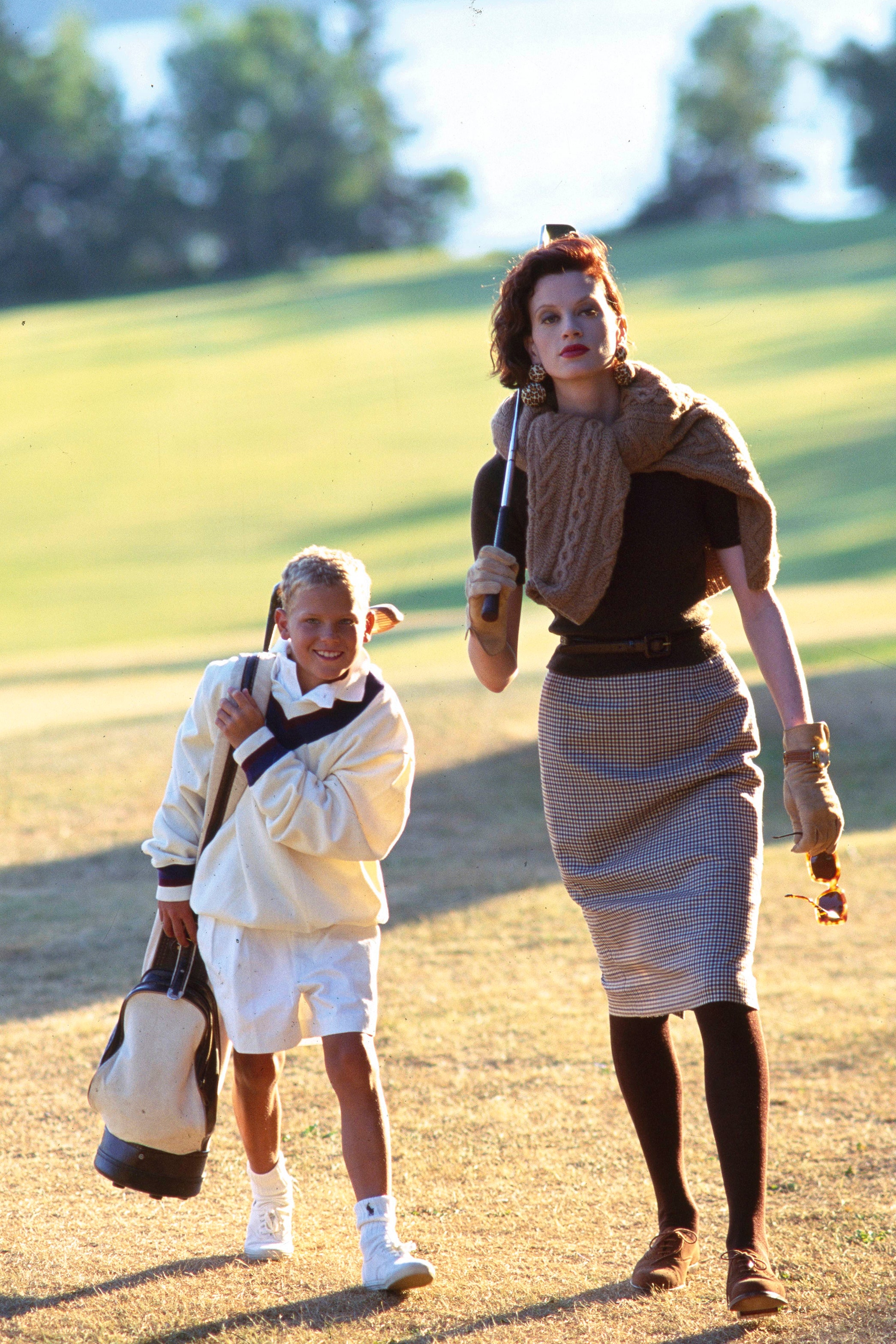 UNSPECIFIED  NOVEMBER 1  Model Kristen McMenamy walking down golf green with young male caddie with a ribbed mock...