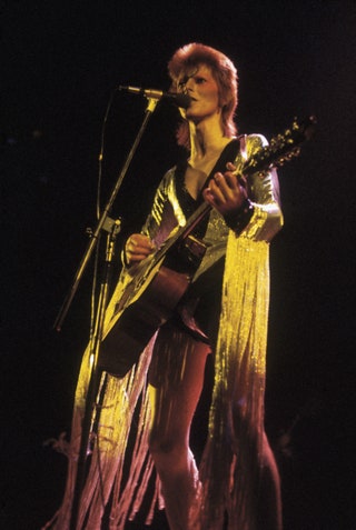 David Bowie performing as Ziggy Stardust at the Hammersmith Odeon 1973. He is wearing a silver costume with gold tassels...