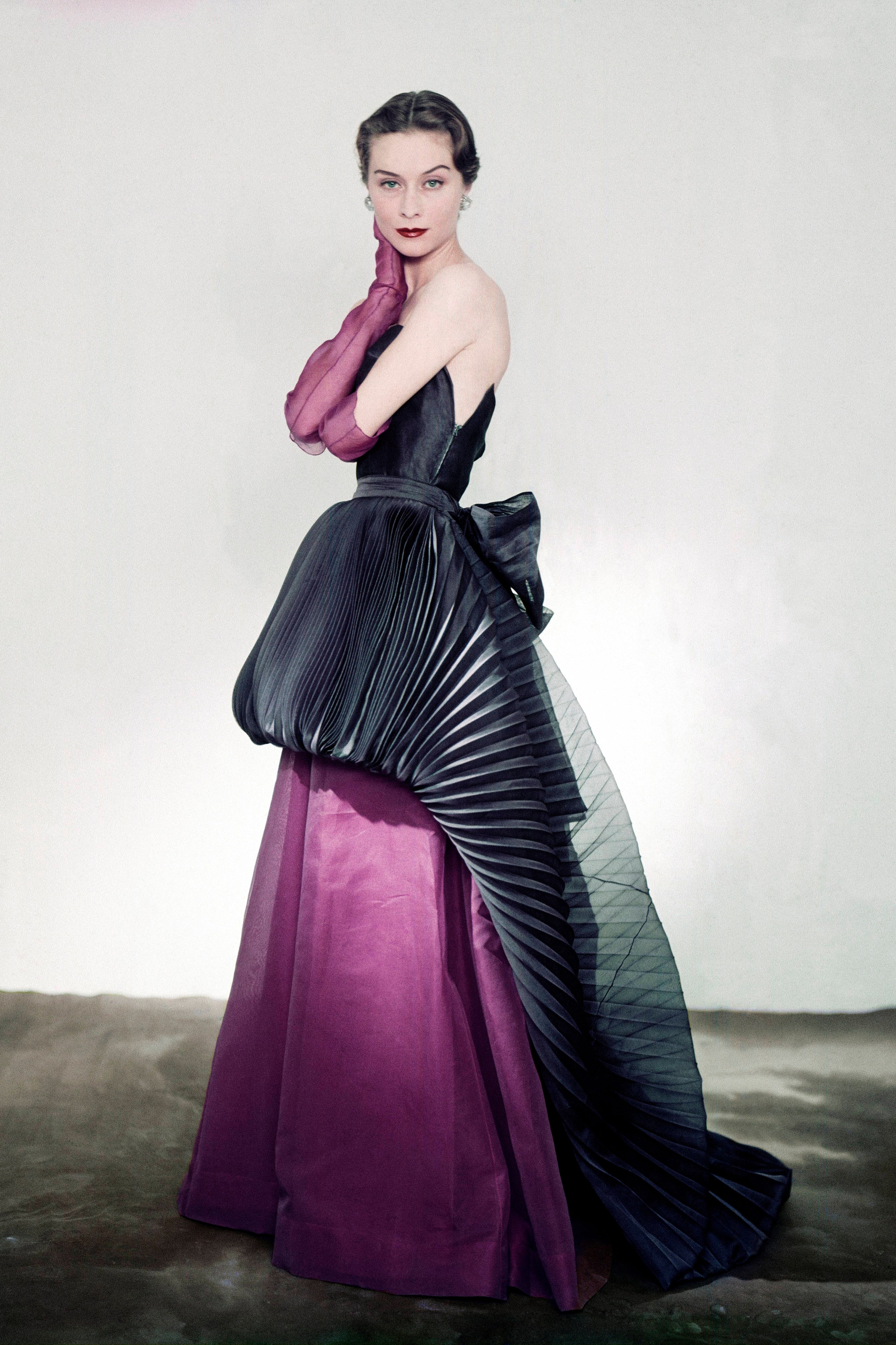 Model wearing Schiaparelli silk organdie strapless purple dress and purple gloves with a navy pleated overskirt apron...