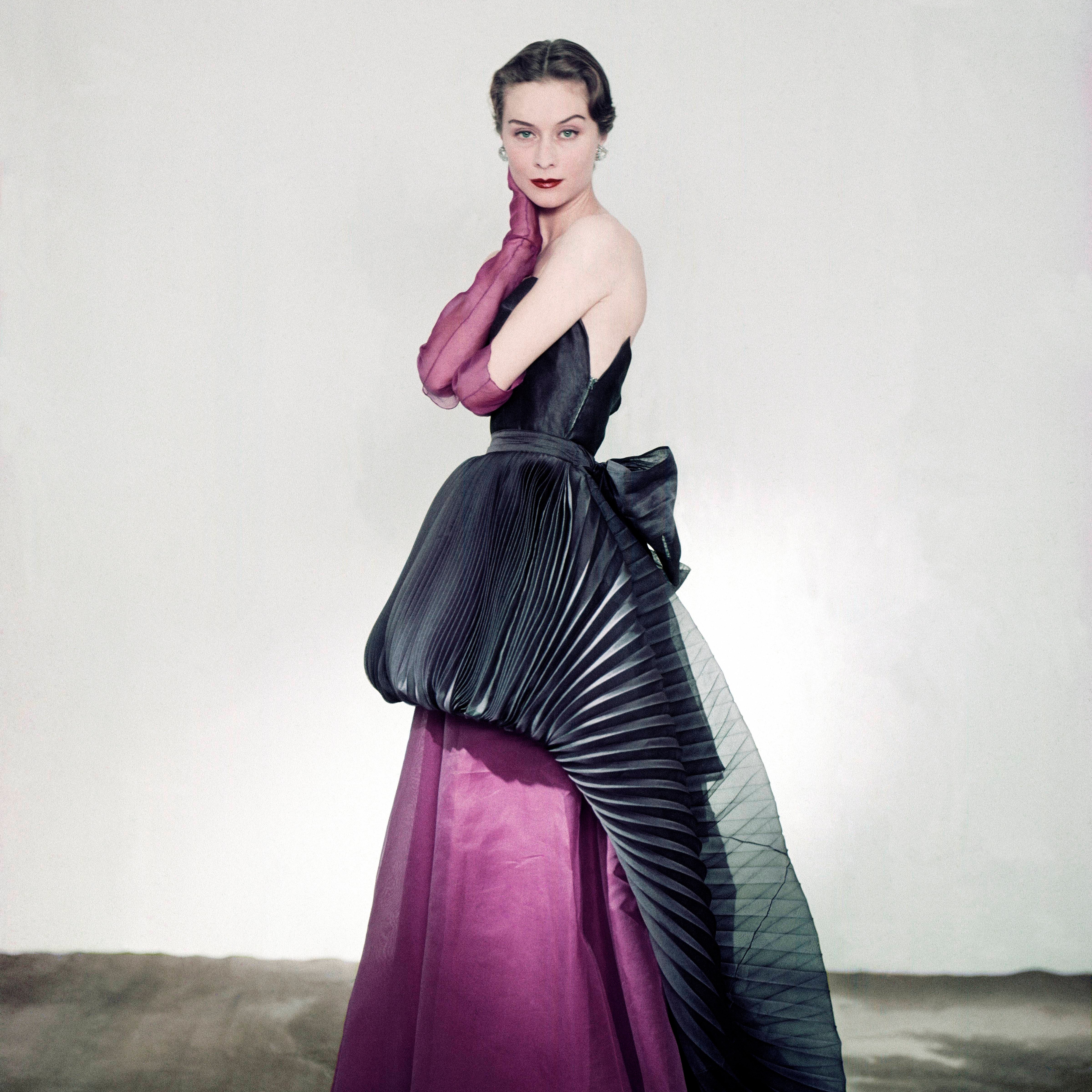 Model wearing Schiaparelli silk organdie strapless purple dress and purple gloves with a navy pleated overskirt apron...