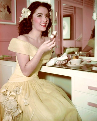 Актриса Элизабет Тейлор наслаждается чаем и пирожным в своей гримерной около 1950 года.