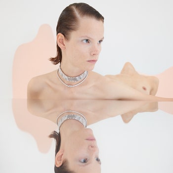 Reflection of topless model wearing choker and short necklace in mirror