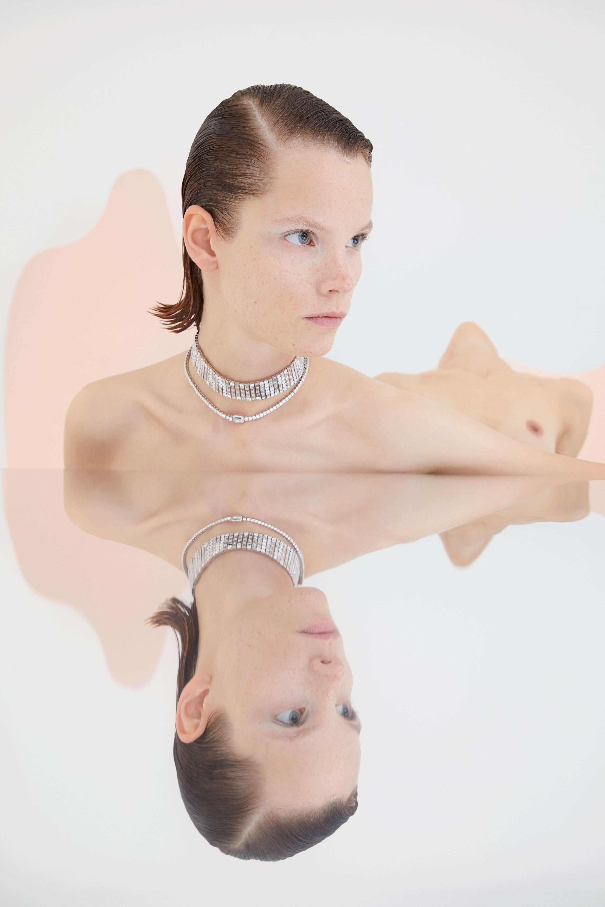 Reflection of topless model wearing choker and short necklace in mirror