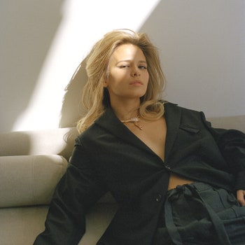 Portrait of actress Lyubov Aksyonova wearing black coloured blazer trousers and necklace sitting on sofa