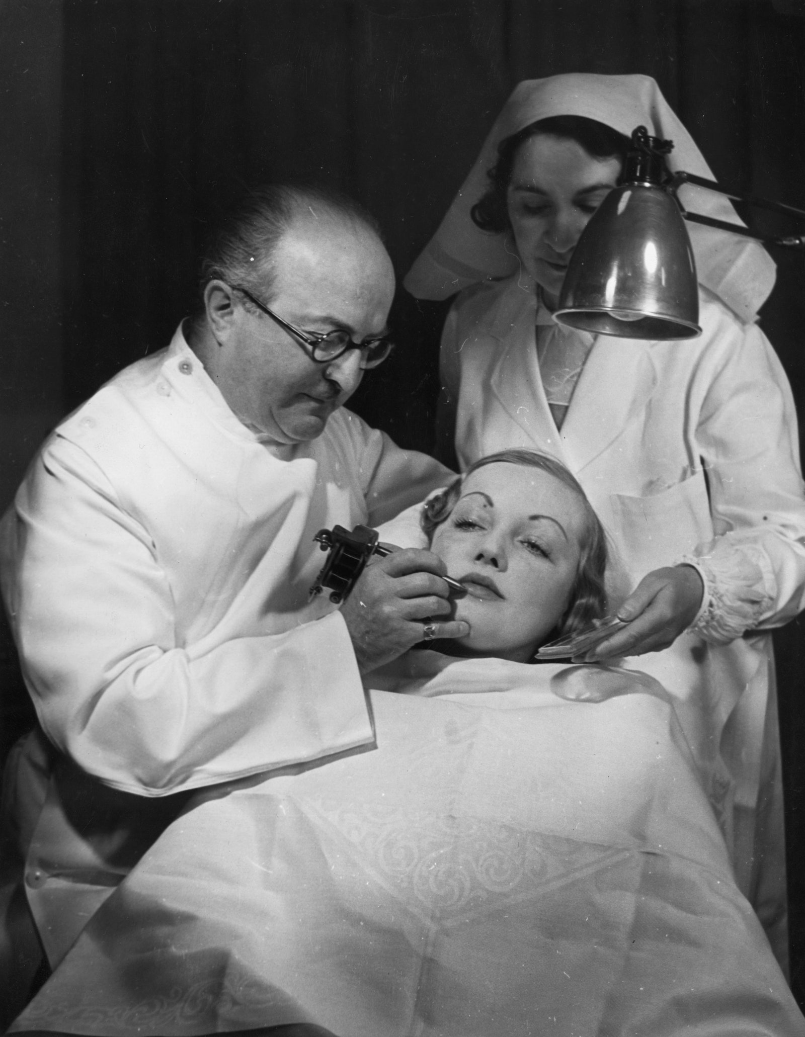 Пластический хирург Джей Си Белл работает над лицом покупательницы в своем салоне красоты 1937 год. Фото Fox Photos ...