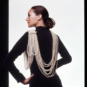 Model Marisa Berenson in back profile shot standing against a white studio backdrop. She is wearing a black dress with...