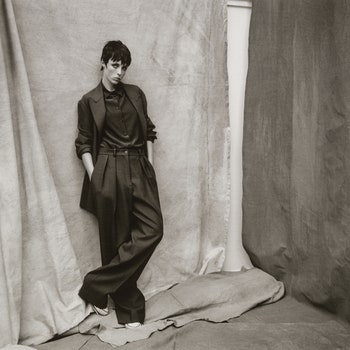 Model with hand in pocket wearing woollen blazer silk shirt trousers and snekaers