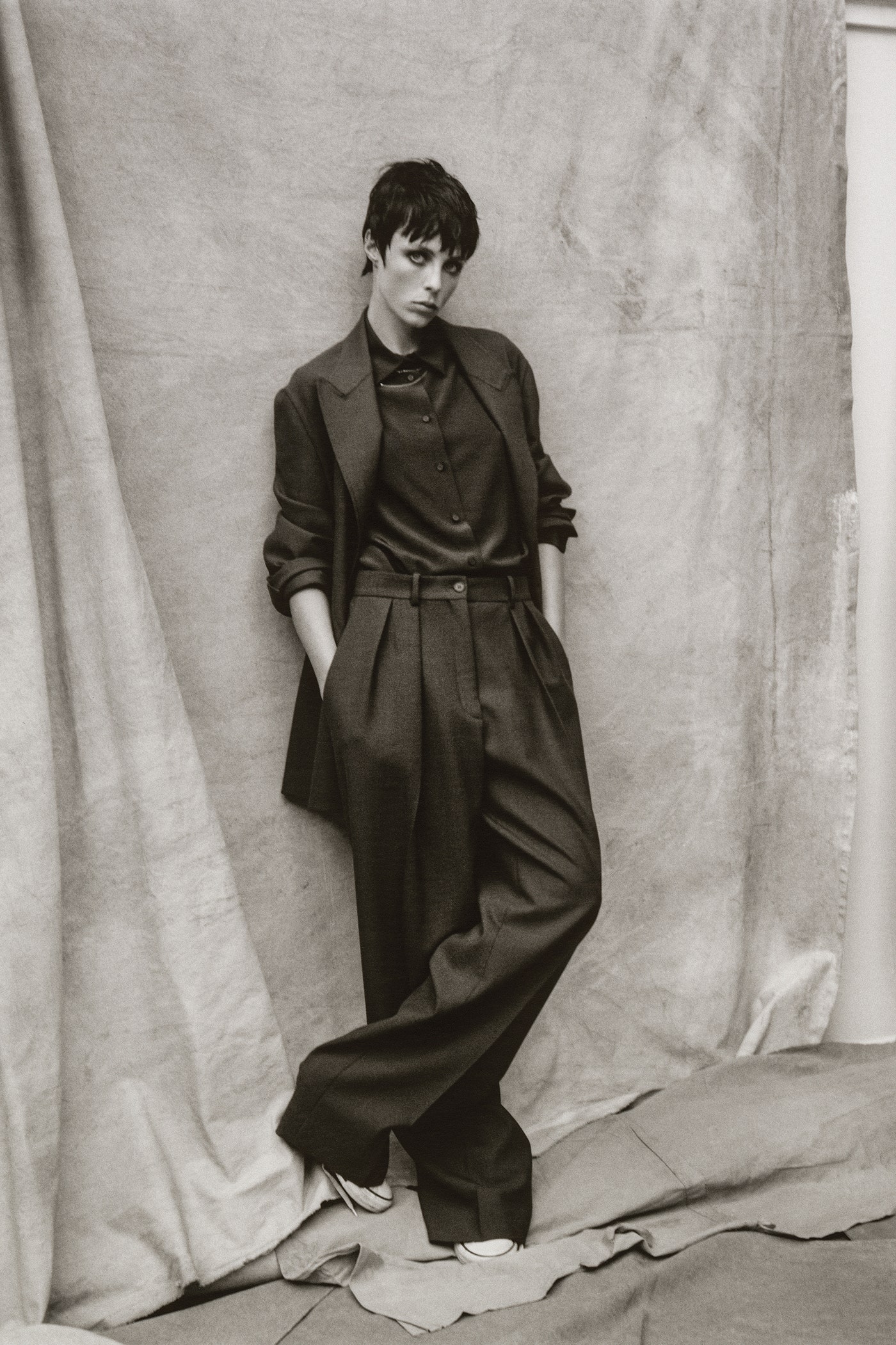 Model with hand in pocket wearing woollen blazer silk shirt trousers and snekaers