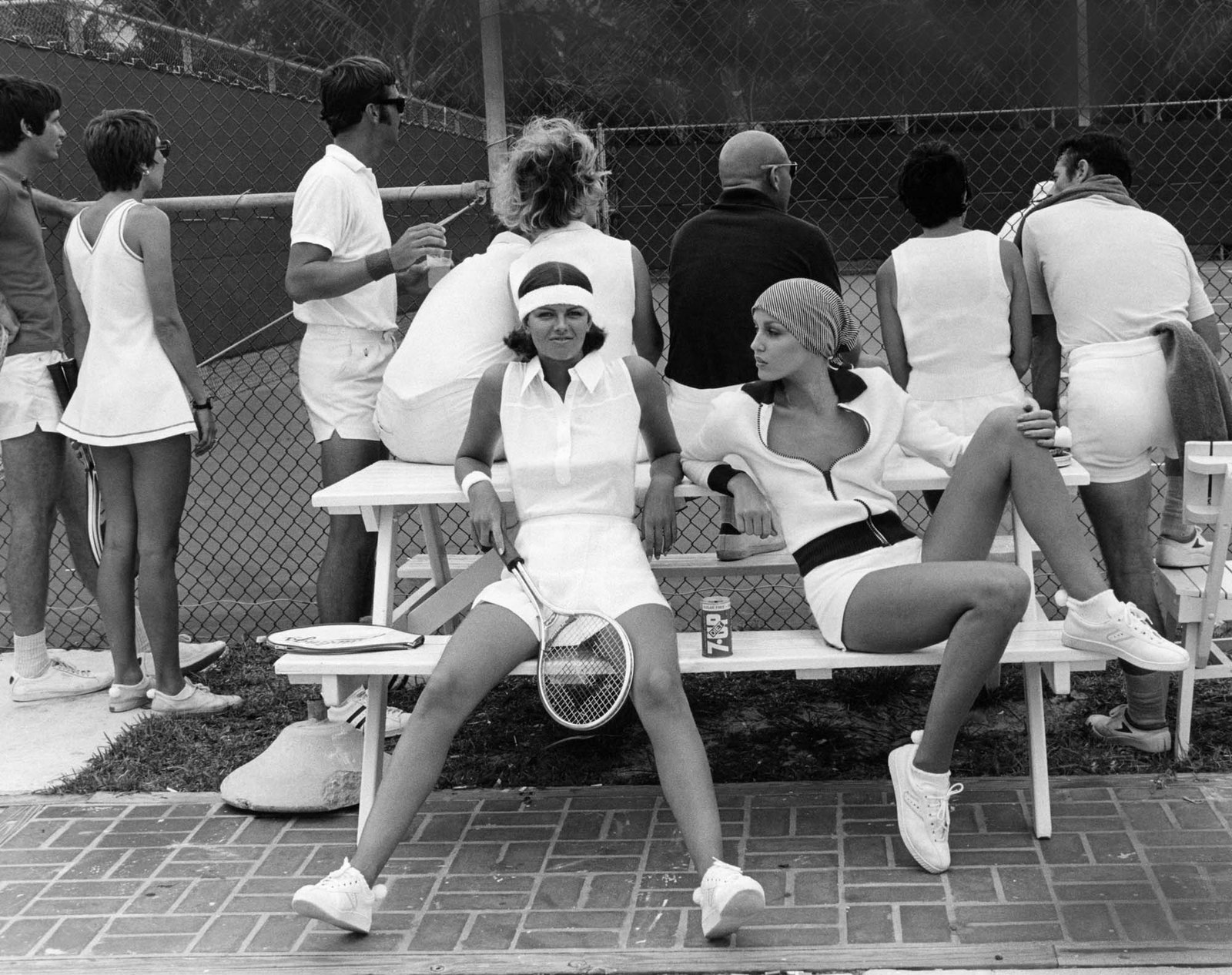 Lisa Taylor y Jerry Hall sentadas en un banco con looks de tenis .