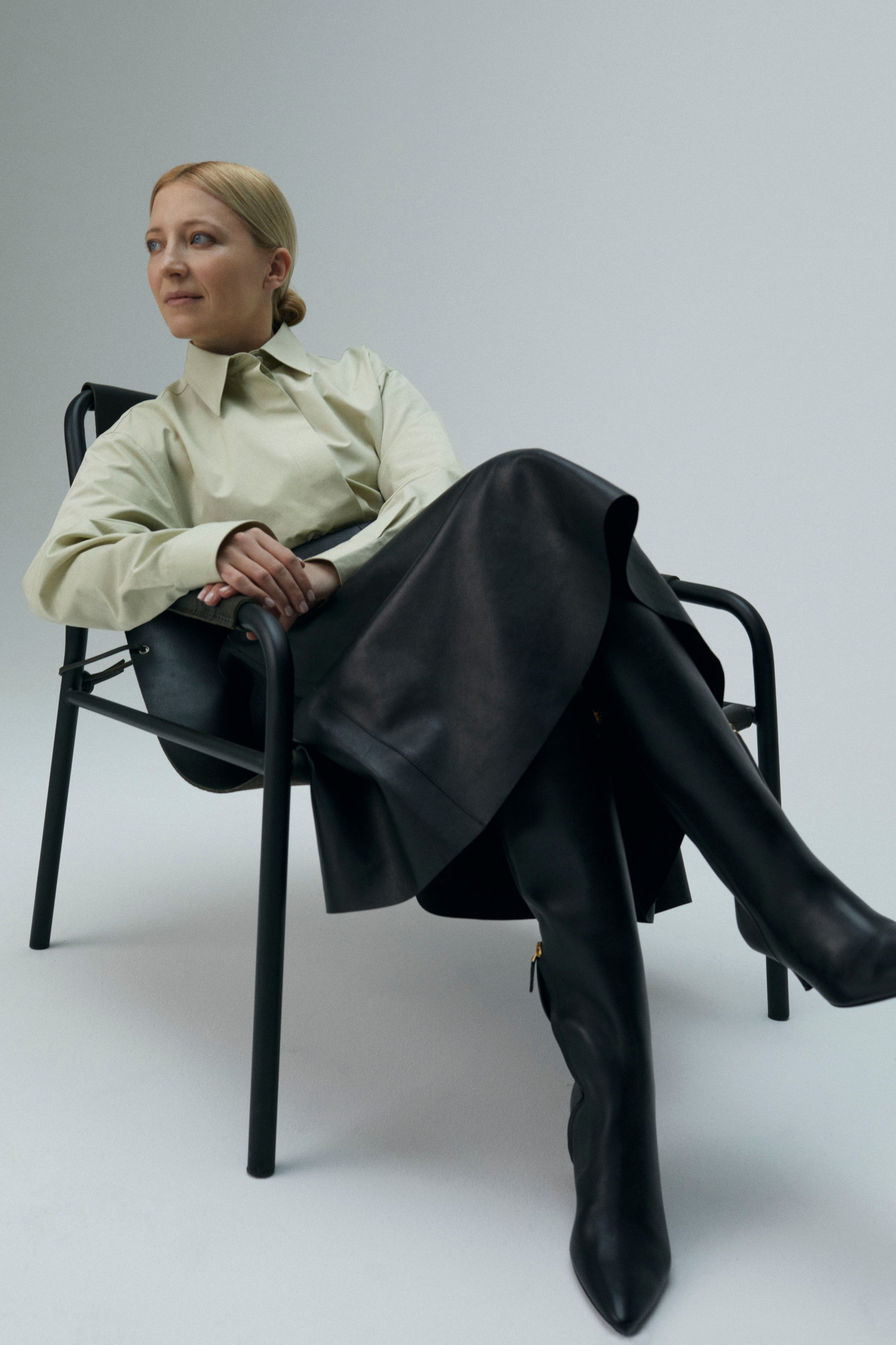 Daria wearing cotton shirt leather skirt and leather boots sitting on chair