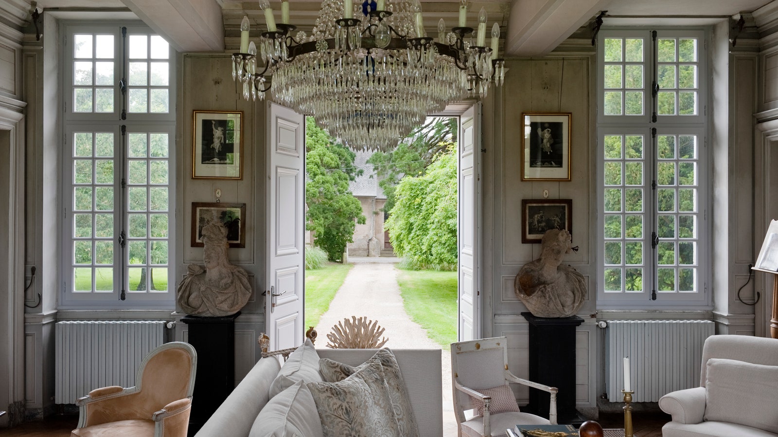 18C chandelier in sitting room furnished with french antiques stone busts and with french doors leading out to the garden